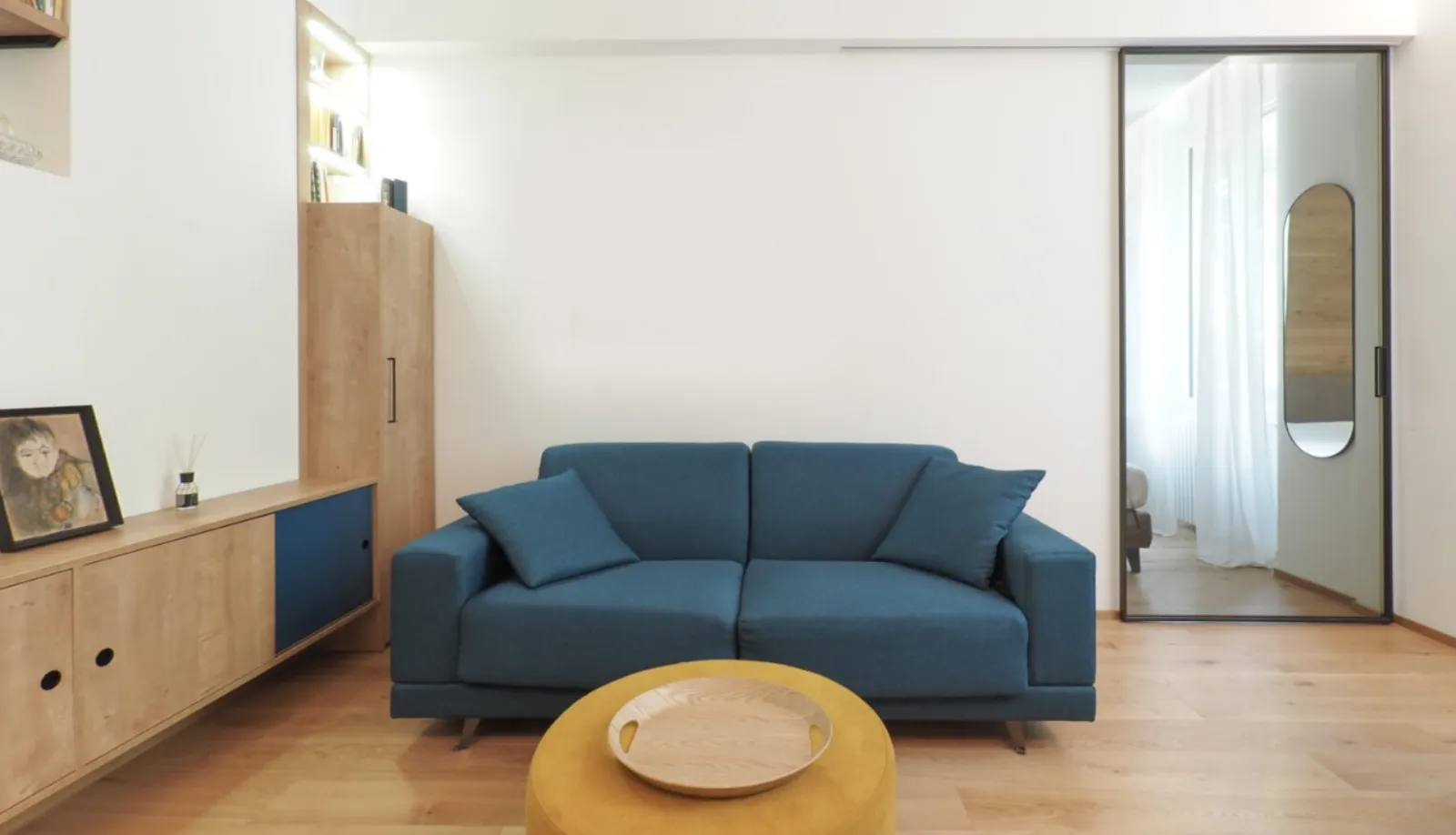 Soggiorno con divano blu, libreria in rovere e vetrata sulla zona notte
