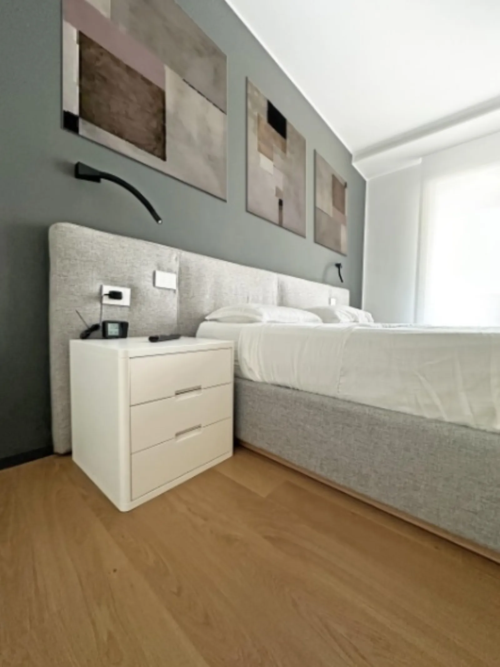 Dettaglio camera da letto con comodino bianco e quadri d'arte