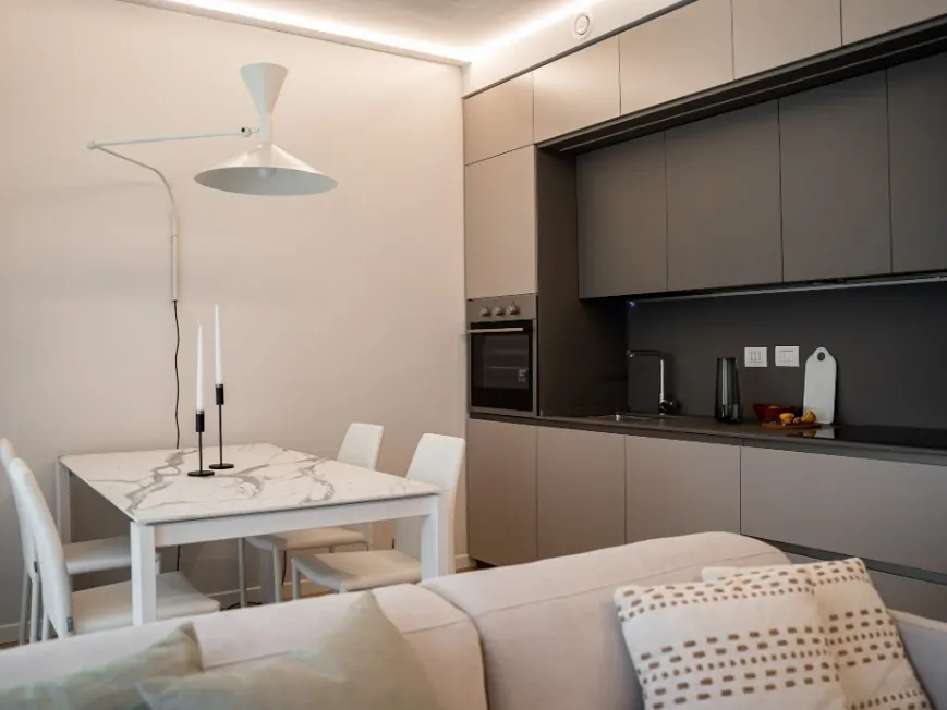 Zona giorno con cucina a vista in finitura tortora e tavolo da pranzo in marmo