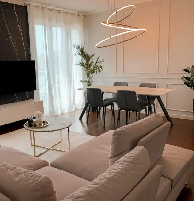 Living con divano grigio chiaro, parete TV in marmo nero e tendaggi velati