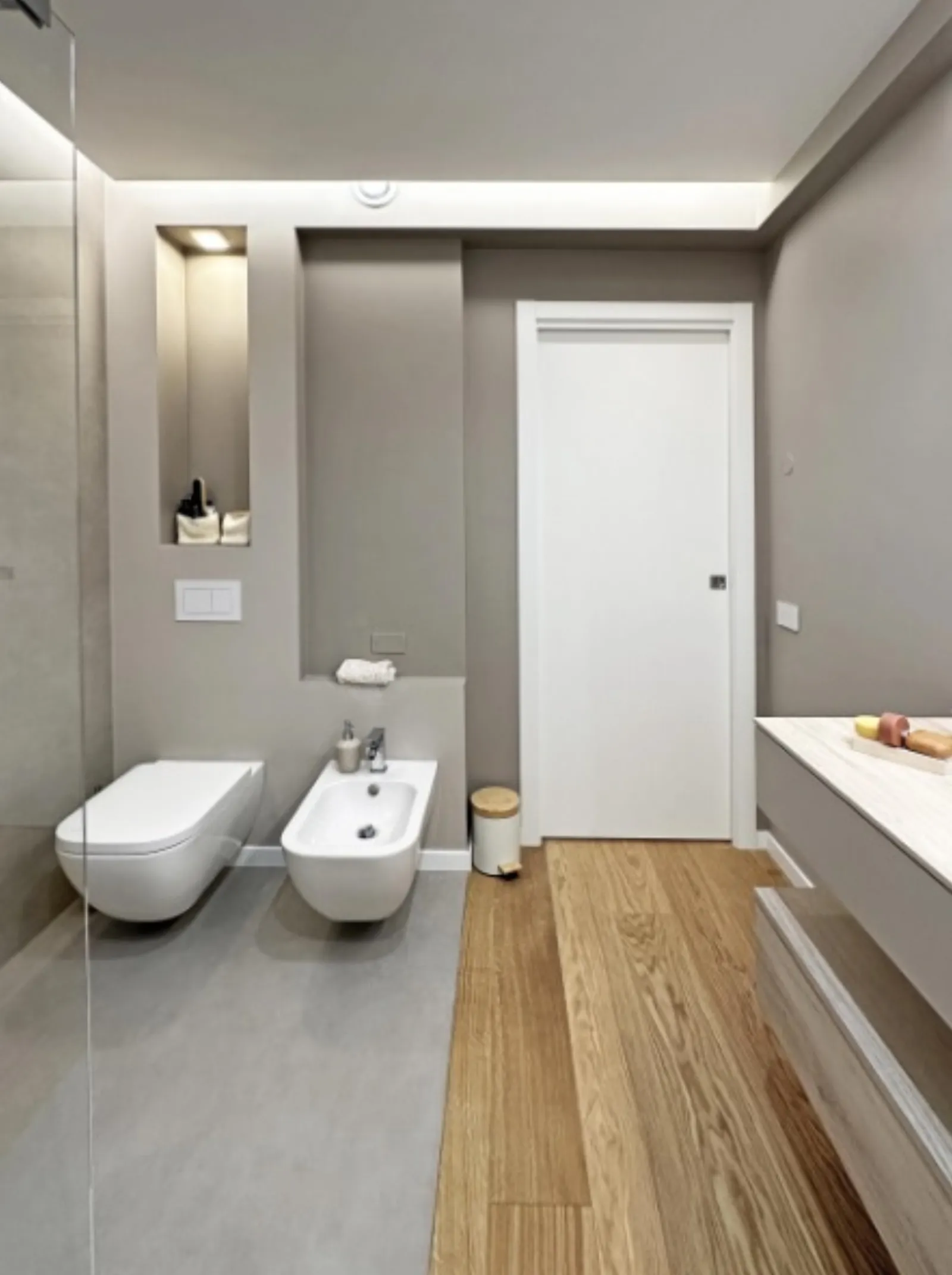 Bagno secondario con sanitari sospesi, nicchia illuminata e pavimento in rovere