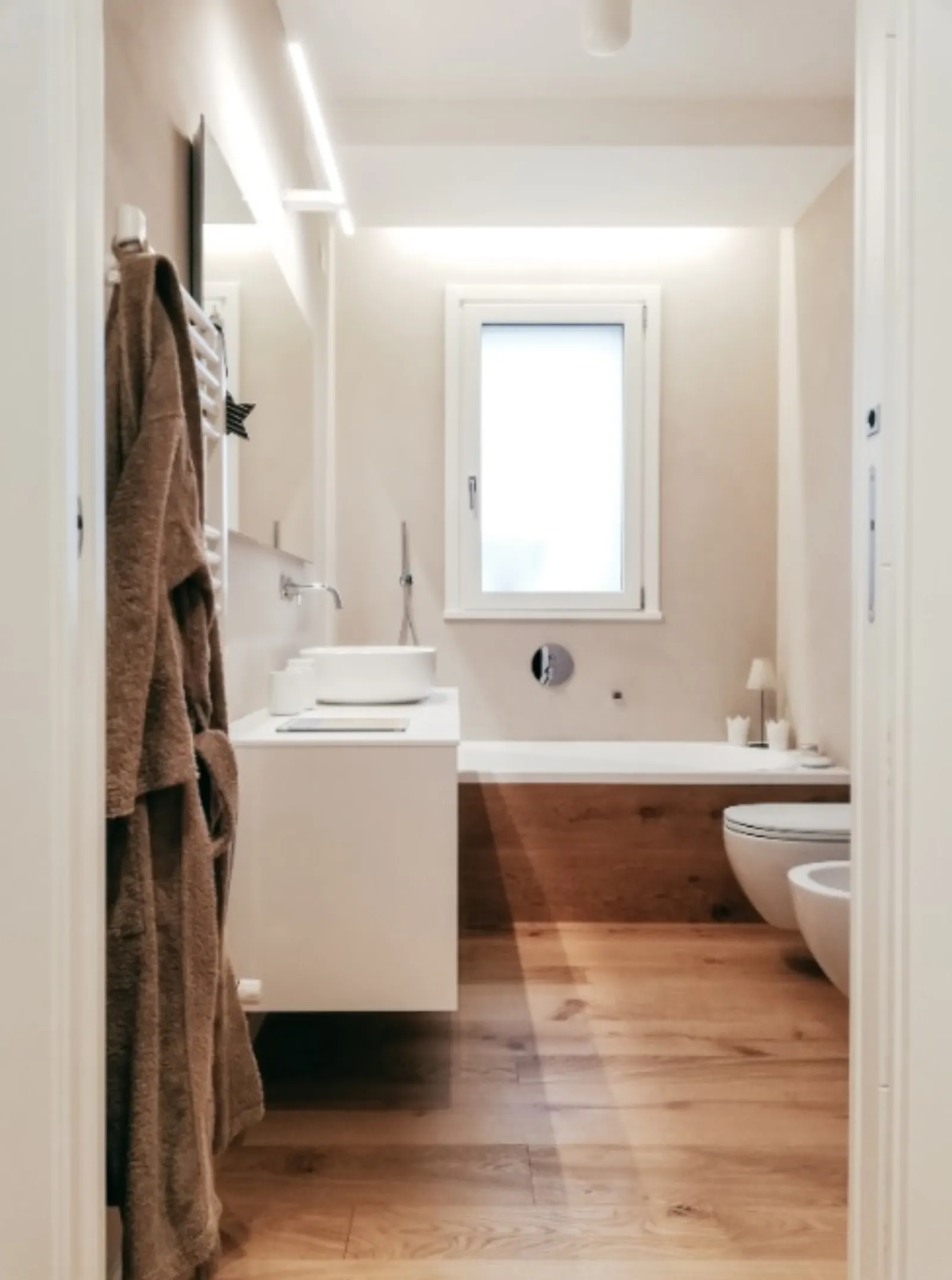 Bagno con vasca incassata, lavabo da appoggio e pavimento in rovere