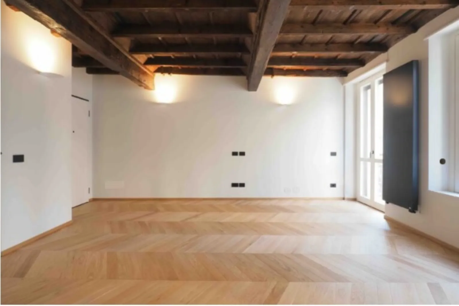 Soggiorno vuoto con soffitto a travi e radiatore antracite