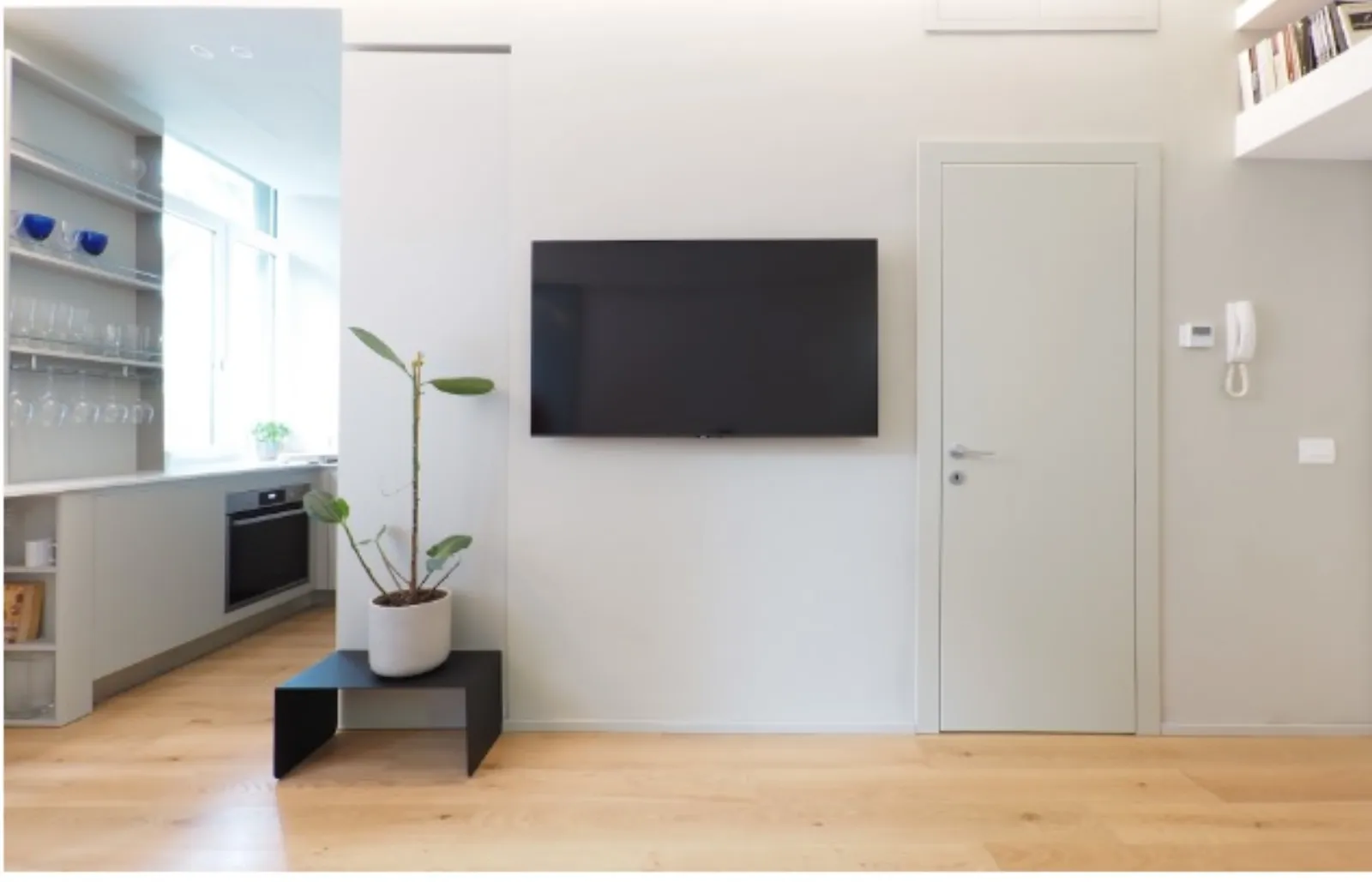 Parete TV con scorcio sulla cucina bianca e libreria a giorno