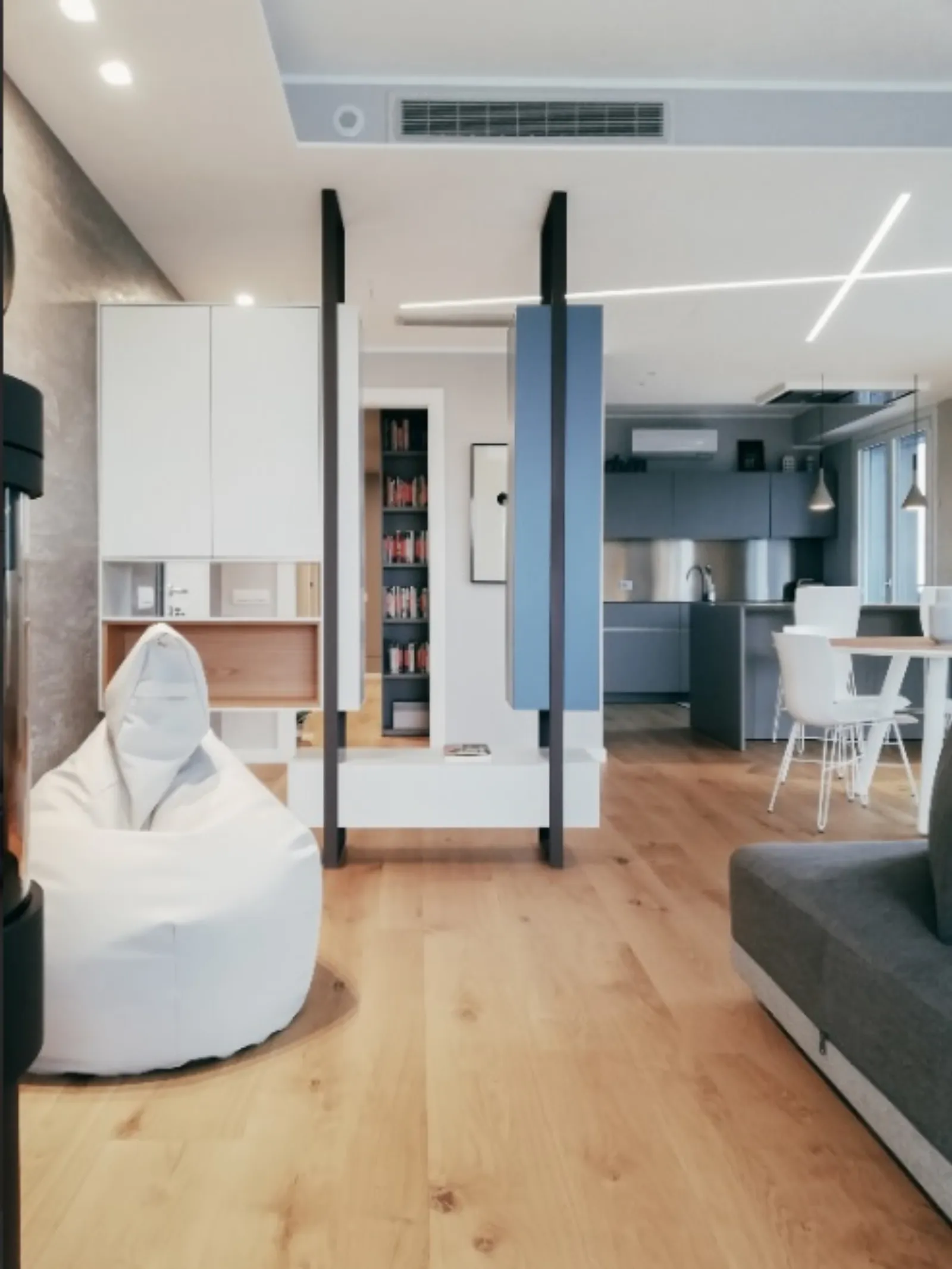 Vista d'insieme con libreria, pouf e cucina sullo sfondo