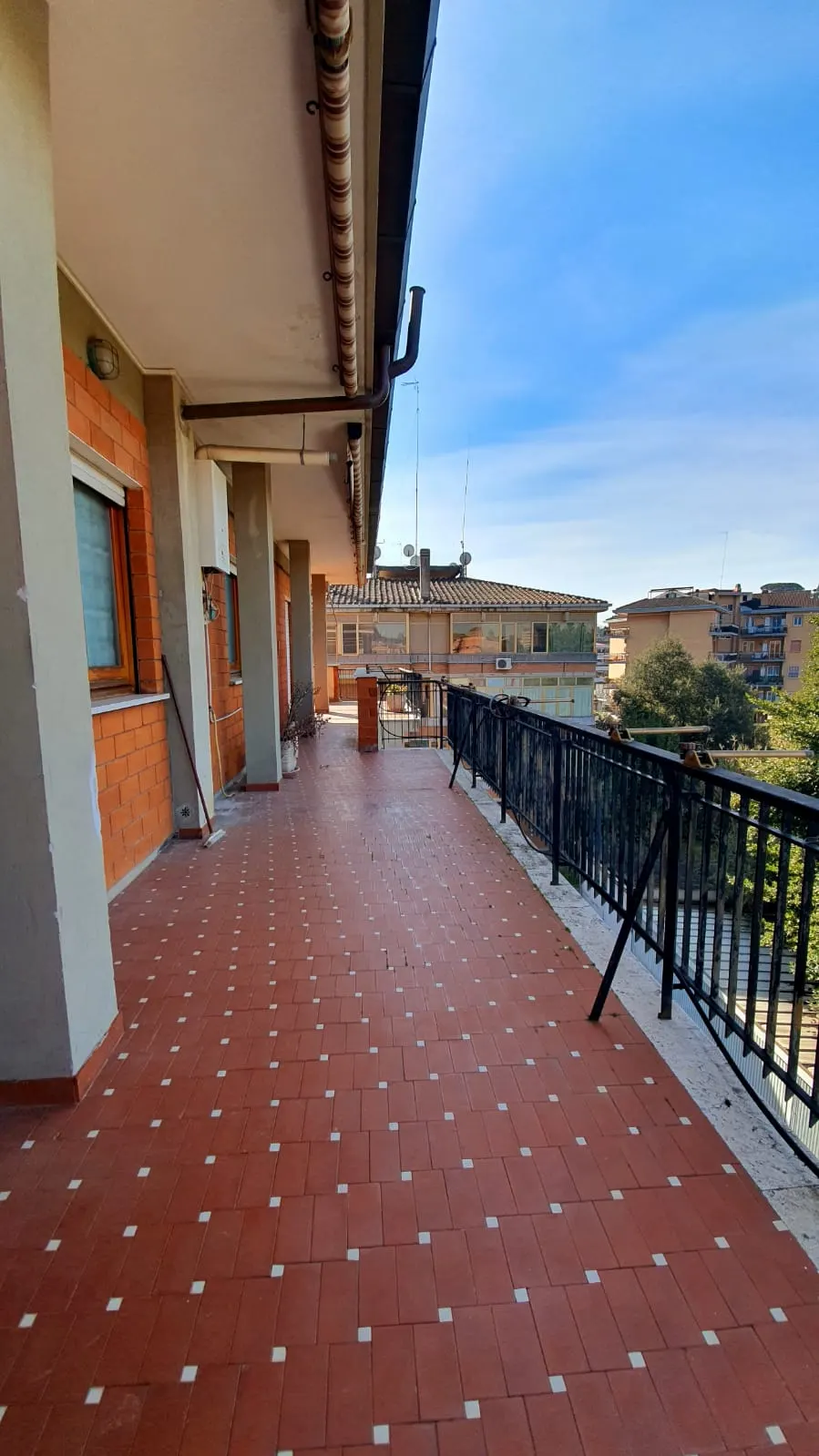 Lungo terrazzo perimetrale con ringhiera in ferro battuto e vista sul quartiere