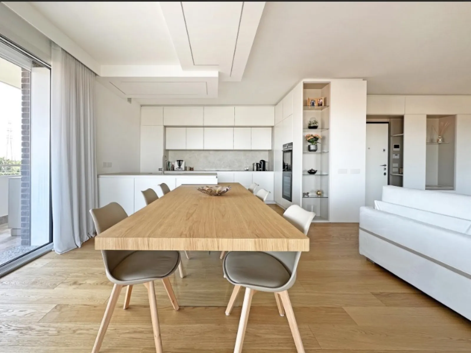 Zona pranzo con tavolo in rovere, cucina bianca a vista e affaccio sul terrazzo