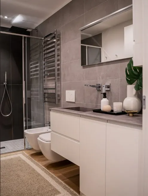 Bagno padronale con rivestimento grigio, doccia e mobile bianco sospeso