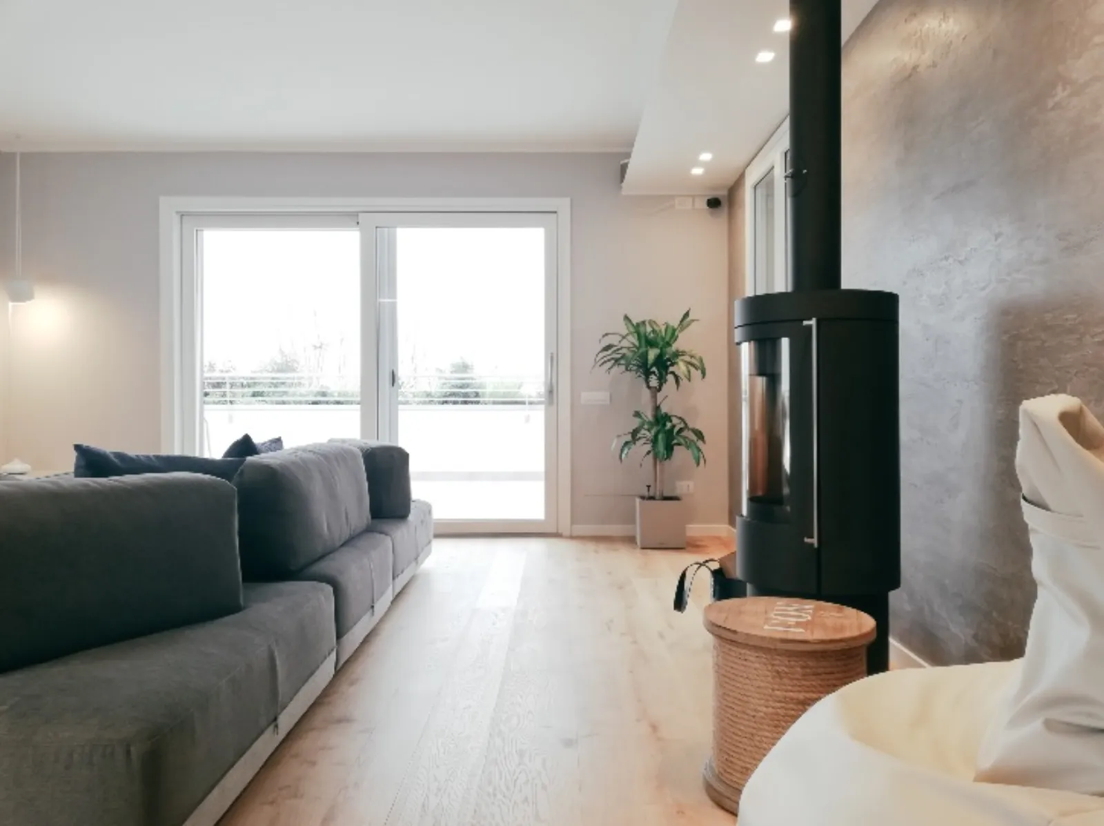 Zona giorno open space con divano grigio, stufa a pellet e grande vetrata sul terrazzo