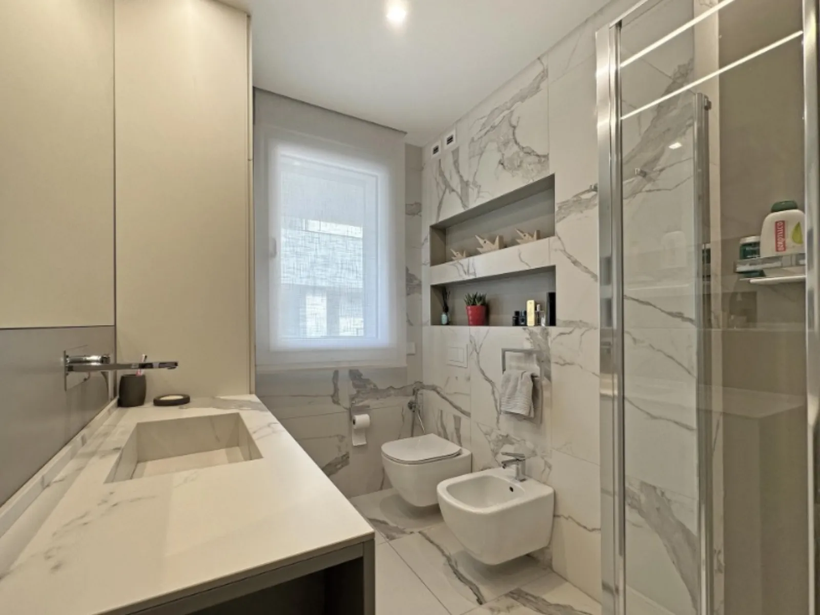 Bagno effetto marmo con nicchie a parete e sanitari sospesi