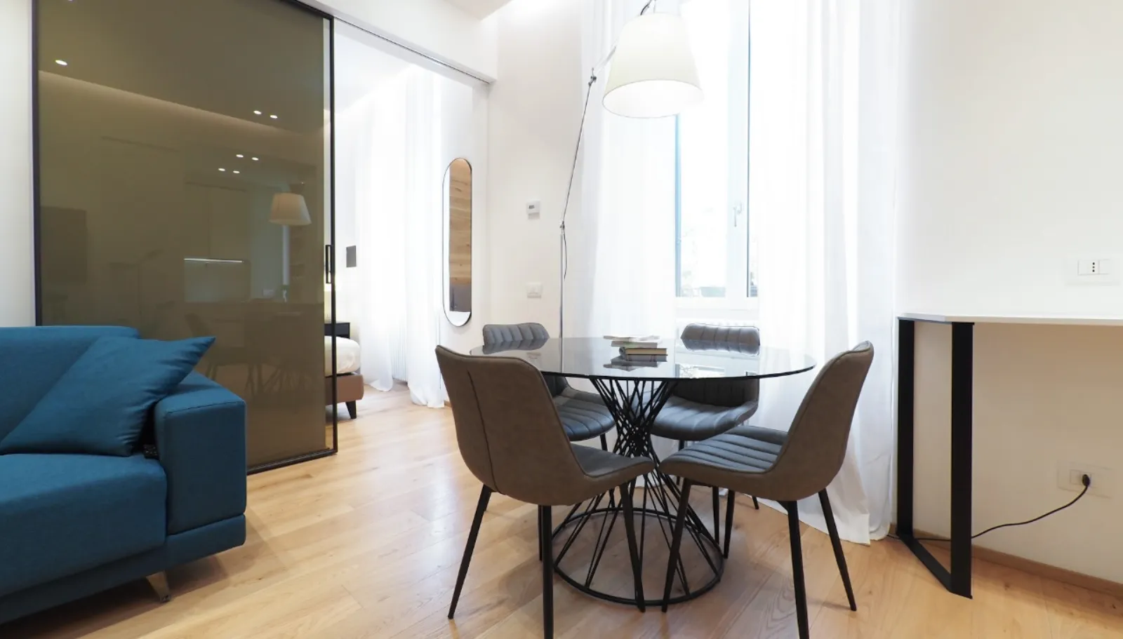 Zona pranzo con lampada ad arco e vetrata scorrevole verso la camera
