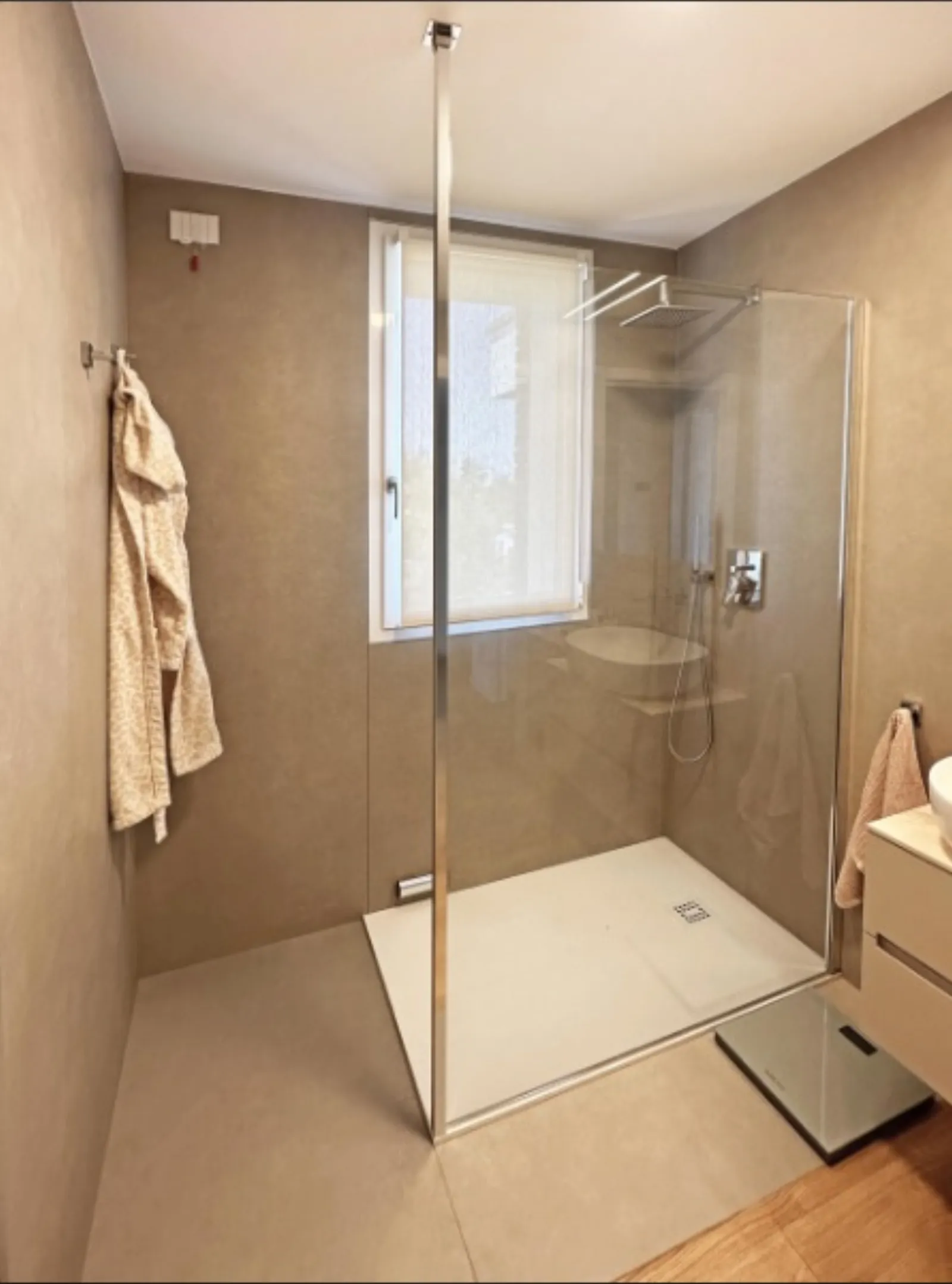 Bagno in microcemento beige con doccia walk-in e vetrata centrale